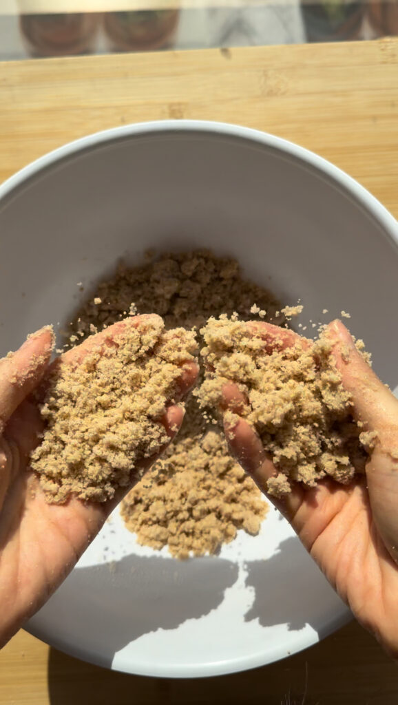 Mixing a brown sugar crumble in a white bowl.