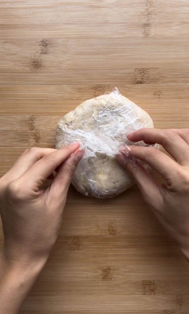 Unwrapping plastic wrap from a disc of pie dough.