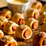Mini pretzel dog bites lined up on a parchment-lined baking sheet.
