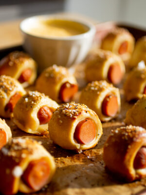 Mini pretzel dog bites lined up on a parchment-lined baking sheet.