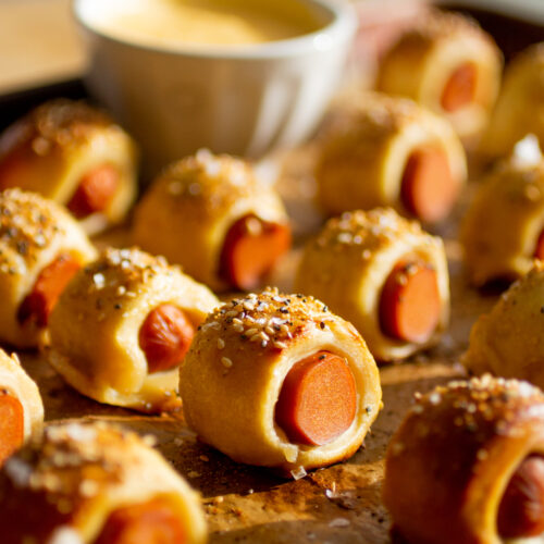 Mini pretzel dog bites lined up on a parchment-lined baking sheet.