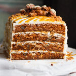 A four layer carrot cake frosted with cream cheese frosting and topped with candied pecans and caramel.