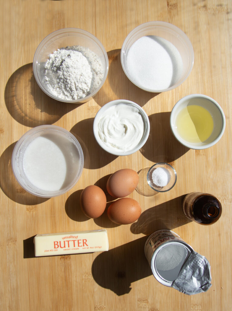 Ingredients laid out on the counter: flour, sugar, coconut milk, sour cream, oil, eggs, butter, salt, vanilla and baking powder.