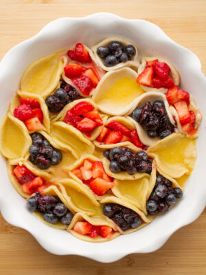 A white pie dish filled with mini red, yellow and blue hand pies.