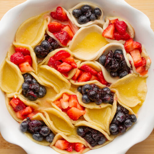A white pie dish filled with mini red, yellow and blue hand pies.