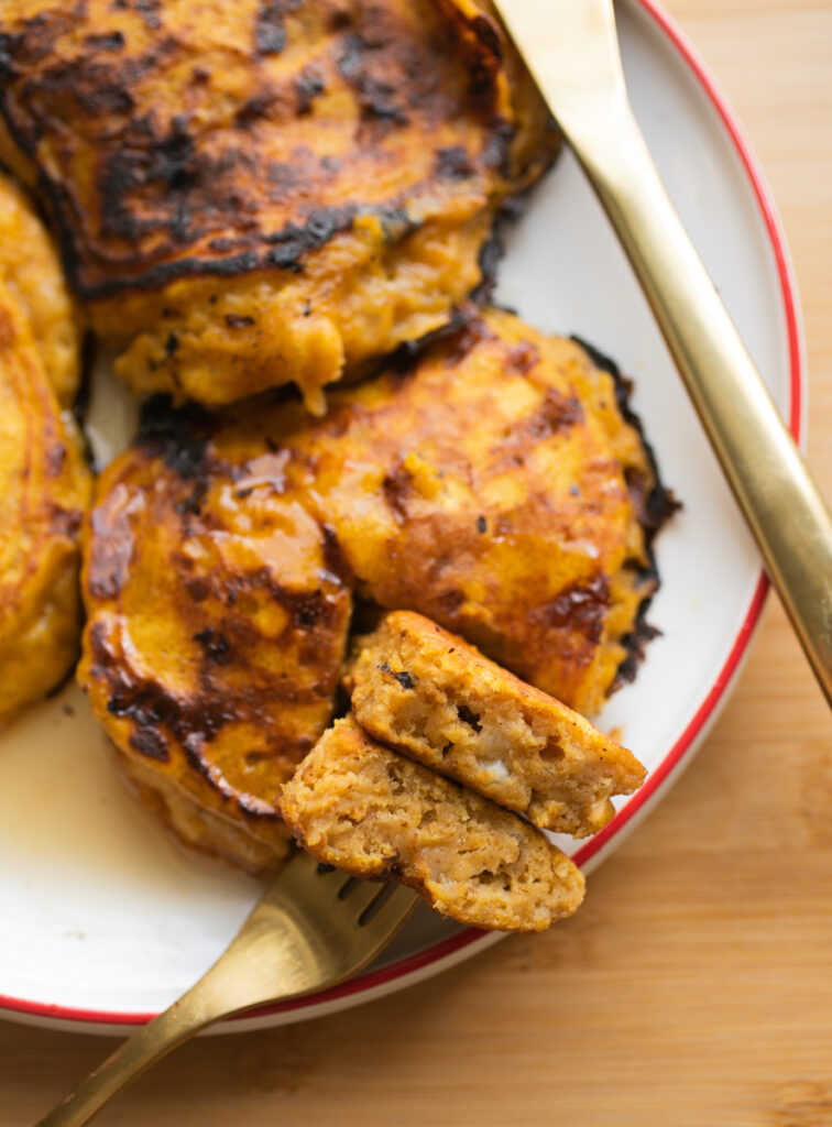 a fork holding up a bite of pumpkin pancakes on a white plate.