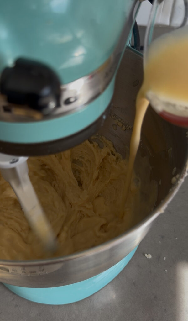 Pouring a milk mixture into the bowl of a stand mixer.