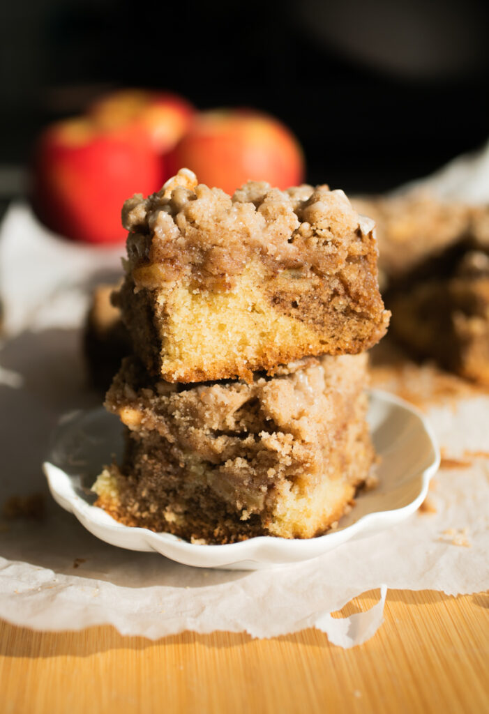 Two squares of apple crumb cake stacked on top of each other on a white plate.