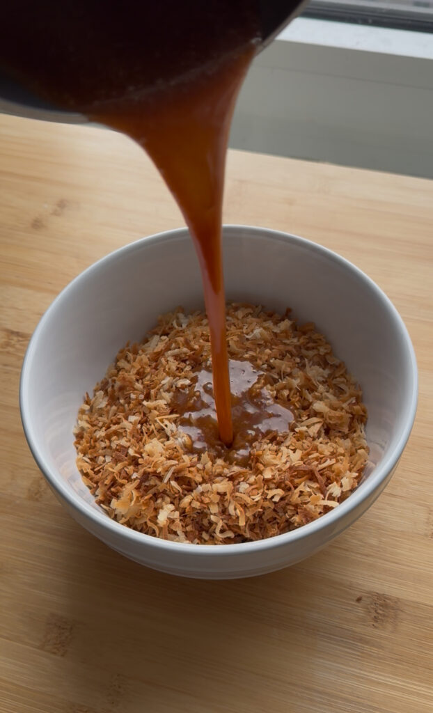 Caramel being poured into a bowl of toasted coconut.