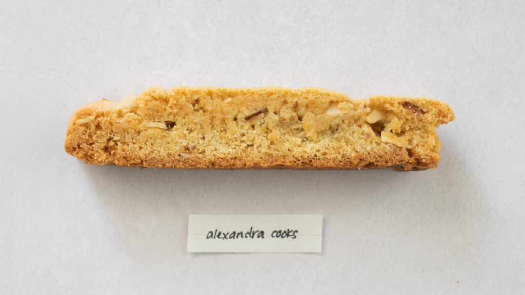 A pice of biscotti on a gray background with the label "Alexandra Cooks."