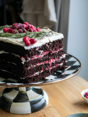 An angled view of a four layer chocolate cake sliced so you can see the layers of cranberry and white frosting between the layers.