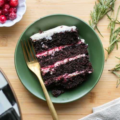 A four-layer slice of chocolate cake with white icing and cranberry compote on a green plate.