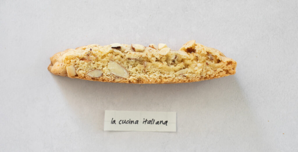 A pice of biscotti on a gray background with the label "La Cucina Italiana."