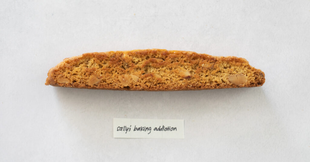 A pice of biscotti on a gray background with the label "Sally's Baking Addiction."