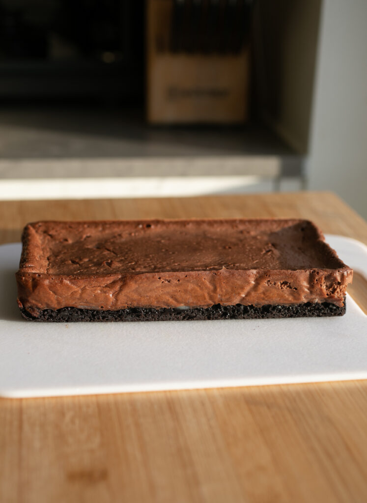 A slab of chocolate cheesecake on a white cutting board.