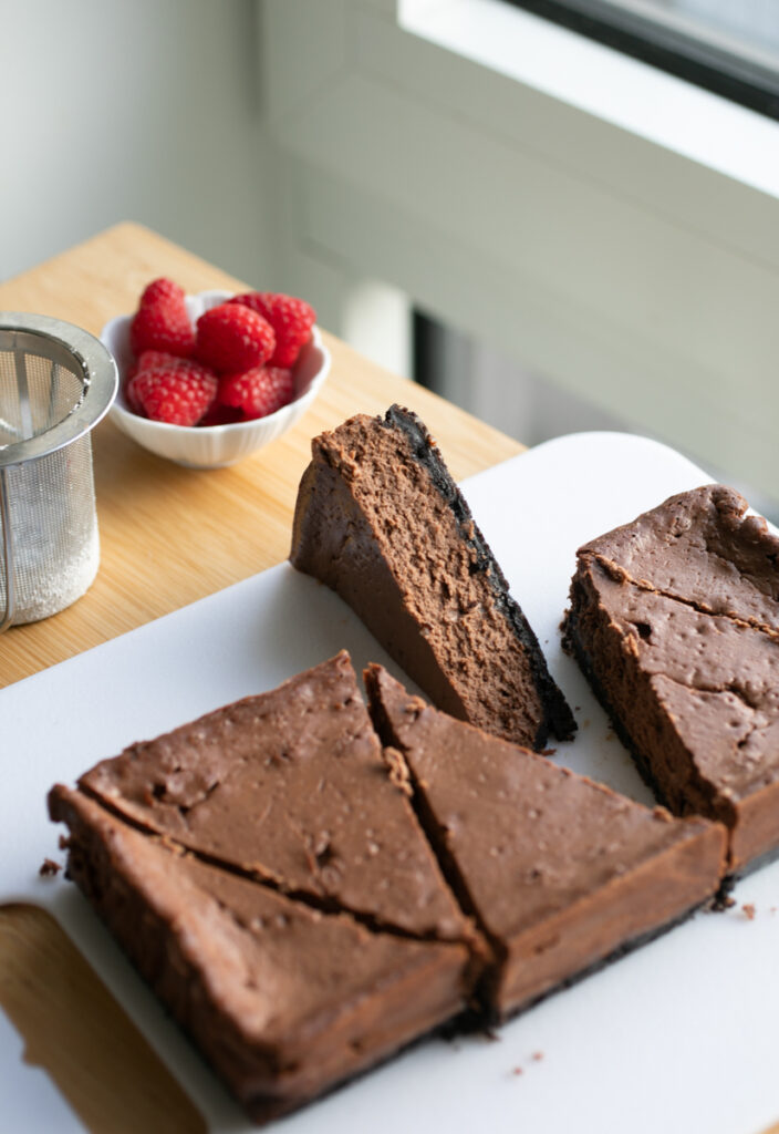 A slab of chocolate cheesecake sliced into triangles on a white cutting board.