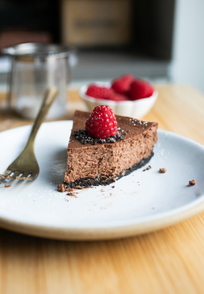 A slice of chocolate cheesecake on a white plate with a bite taken out of it to show the creamy texture.