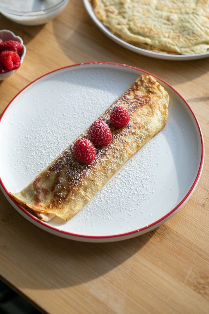 A rolled crepe with raspberries on a plate.