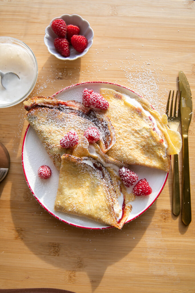 Three crepes with raspberries on a white plate.