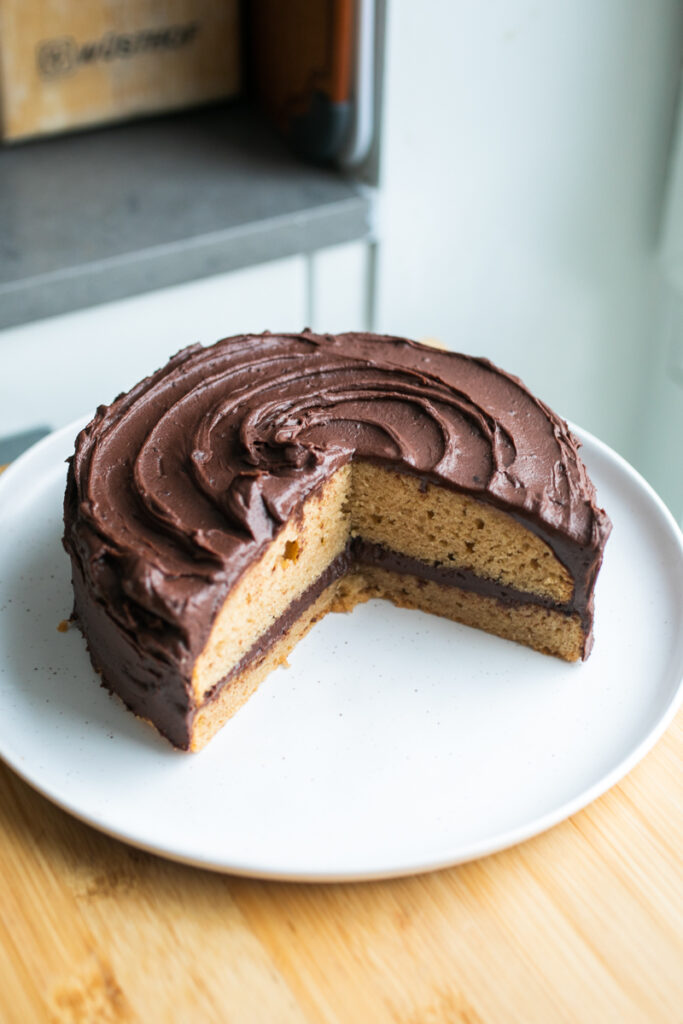 A frosted chocolate peanut butter cake on a white plate with a slice taken out.