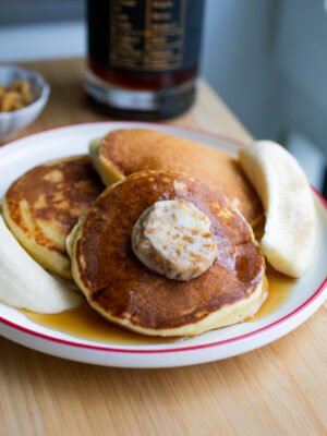 Three fluffy pancakes on a plate with banana halves.